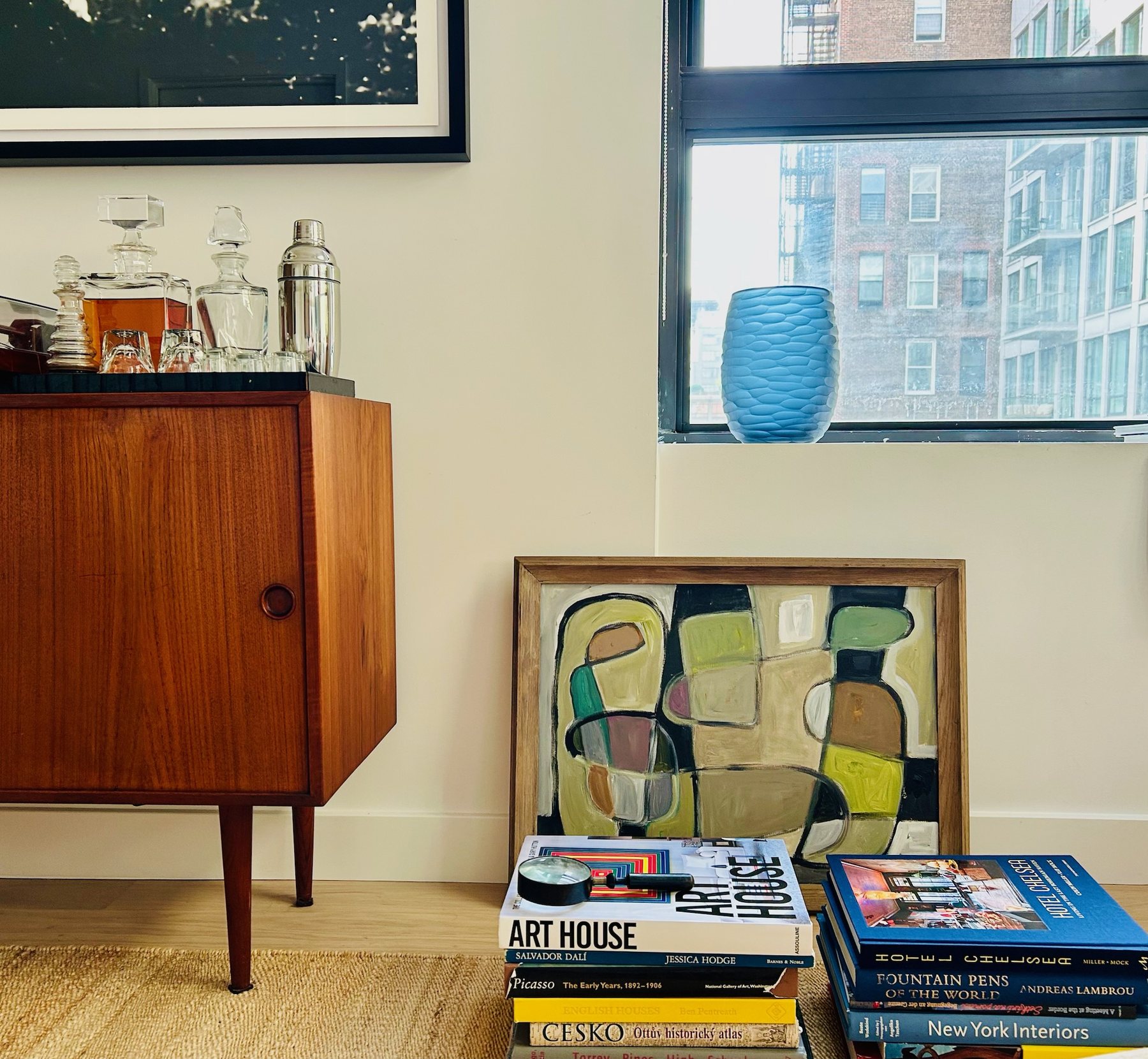 Teak credenza with decanters, beside a framed abstract painting resting on the floor