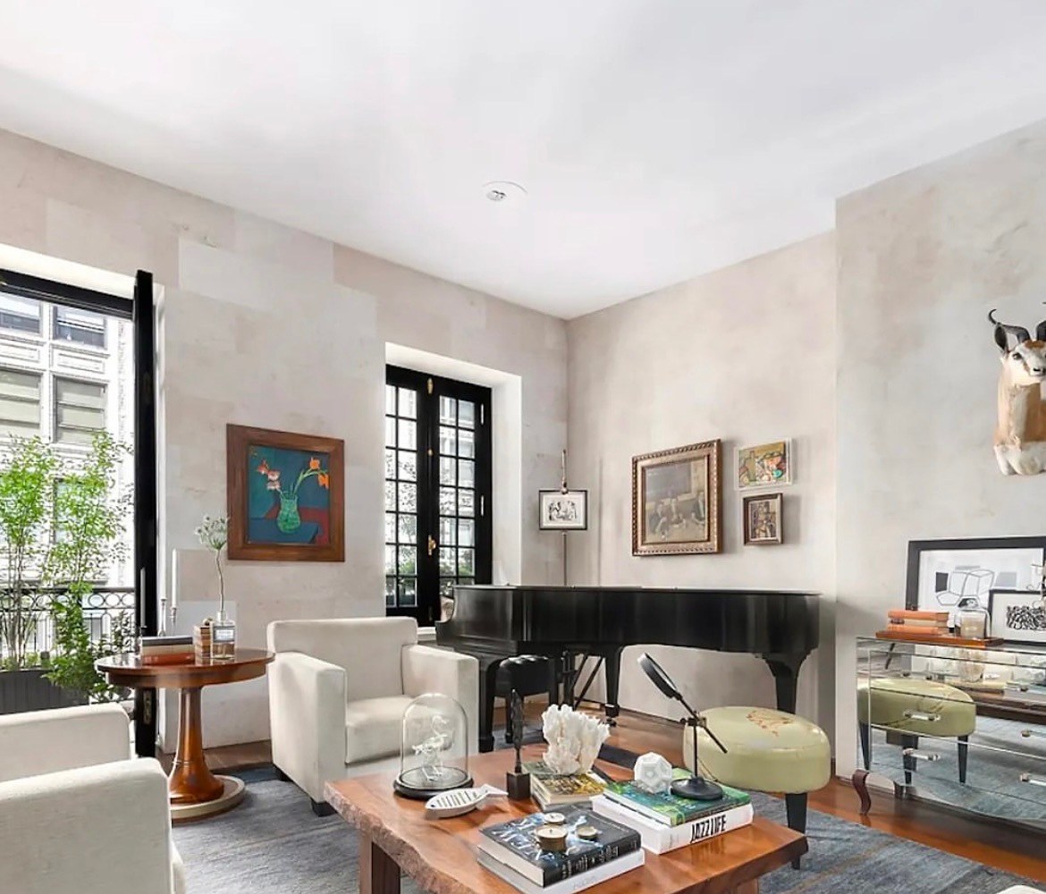 Living room with a grand piano, plaster walls, cream armchairs and a live-edge coffee table