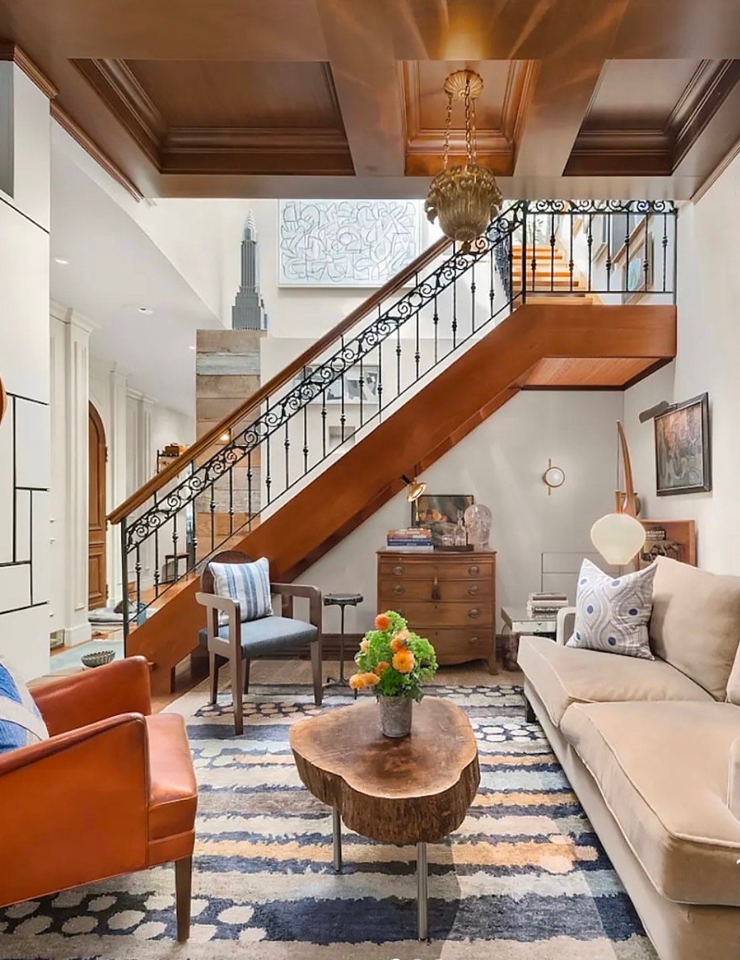 Double-height stair hall with an iron balustrade, coffered wood ceiling and a mahogany chest