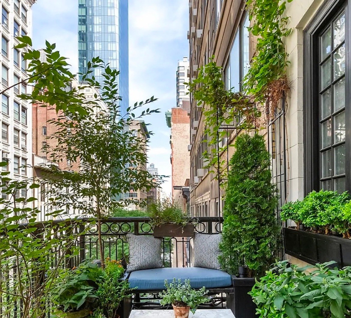 Planted terrace with a checkerboard stone floor, iron bench and a view down the avenue