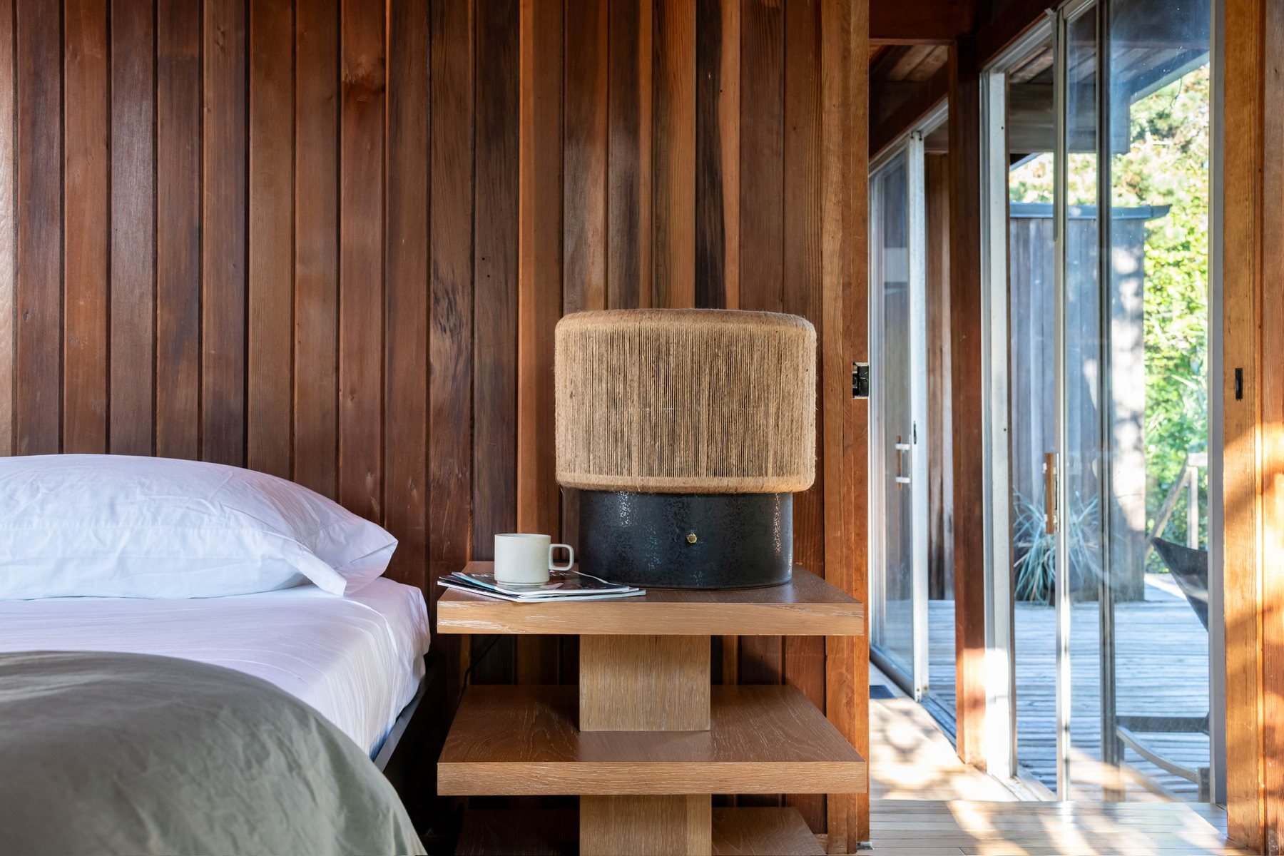 Bedroom with white linens and an oak nightstand beside sliding doors opening to the deck